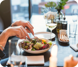 A person enjoying a fresh salad with a fork and knife at a dining table.